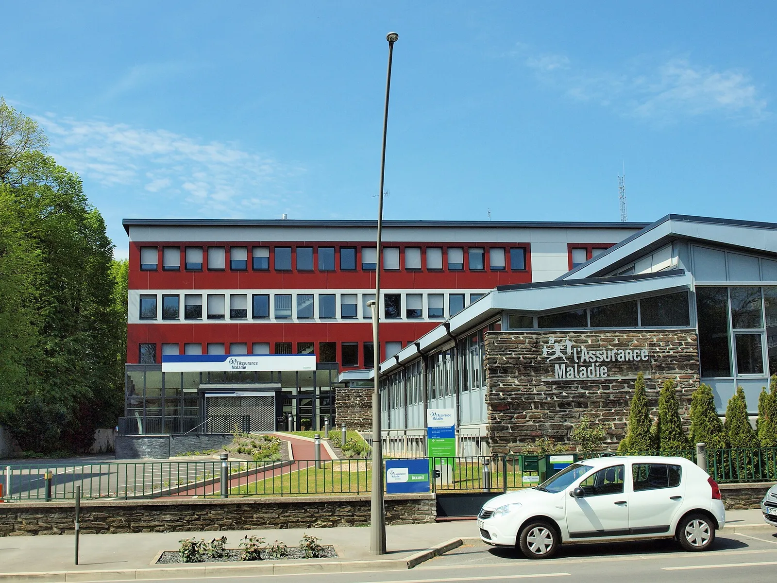 The Assurance Maladie (CPAM) office in Charleville-Mézières, a red and grey building under a blue sky