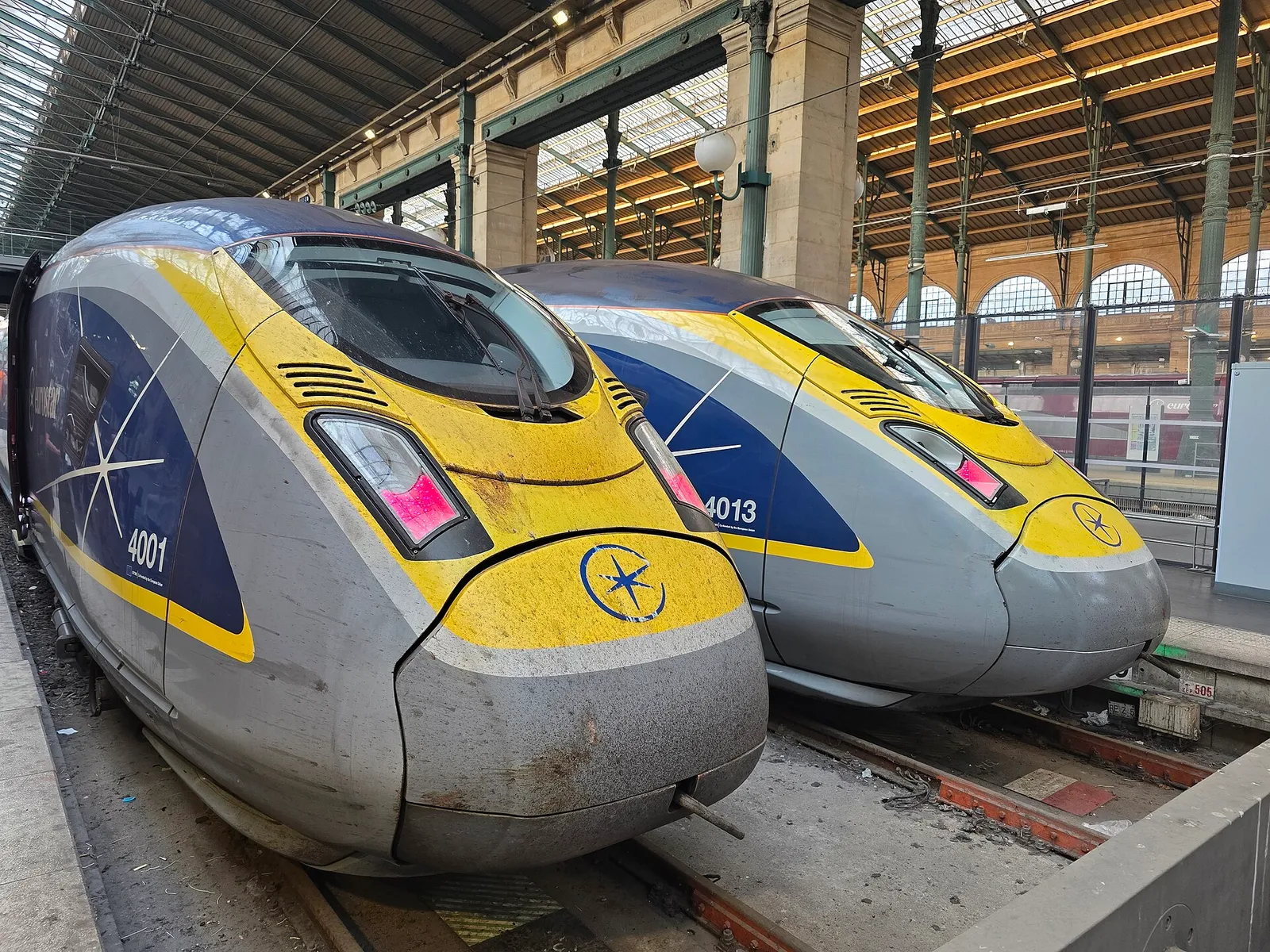 Two Eurostar trains with yellow noses side by side under the iron roof of the Gare du Nord in Paris
