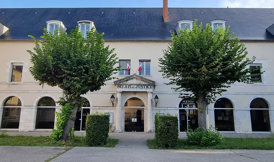 Front of the courthouse in Montargis, with its entrance set into a row of arches and trimmed trees in front.