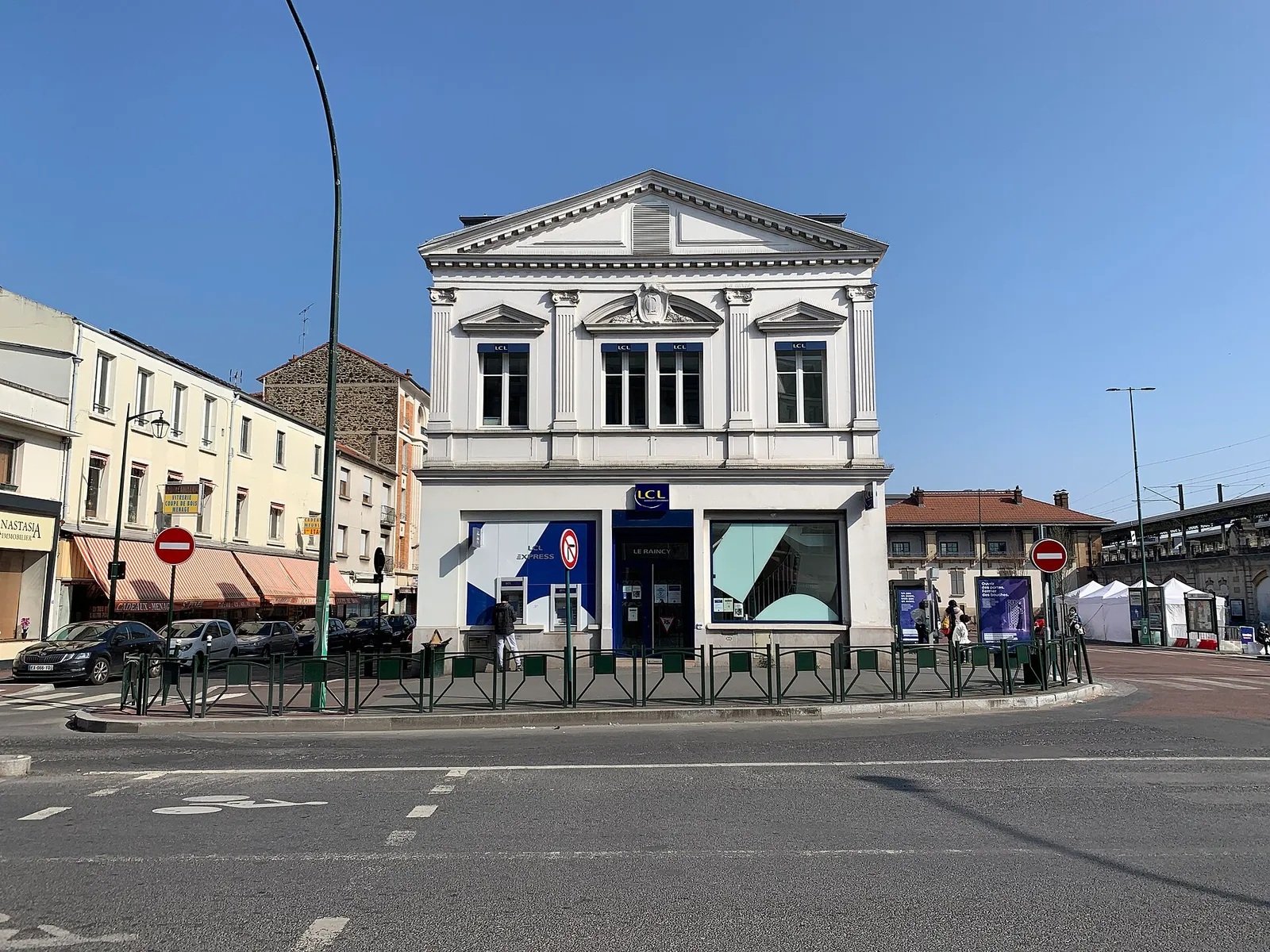 A neoclassical corner building with a triangular pediment housing an LCL bank branch, on a street corner in Le Raincy under a blue sky