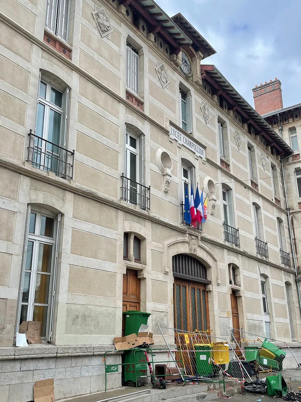 The façade of the Lycée Champollion in Grenoble on September 30, 2026, with bins and metal barriers piled in front of the doors