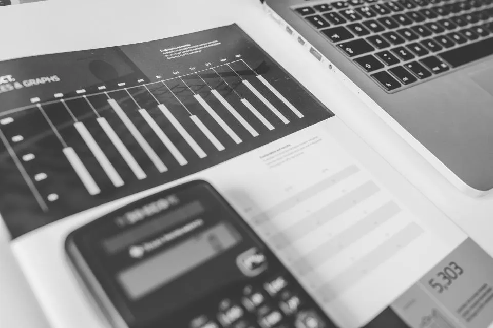 A calculator on printed charts next to a laptop keyboard, in black and white
