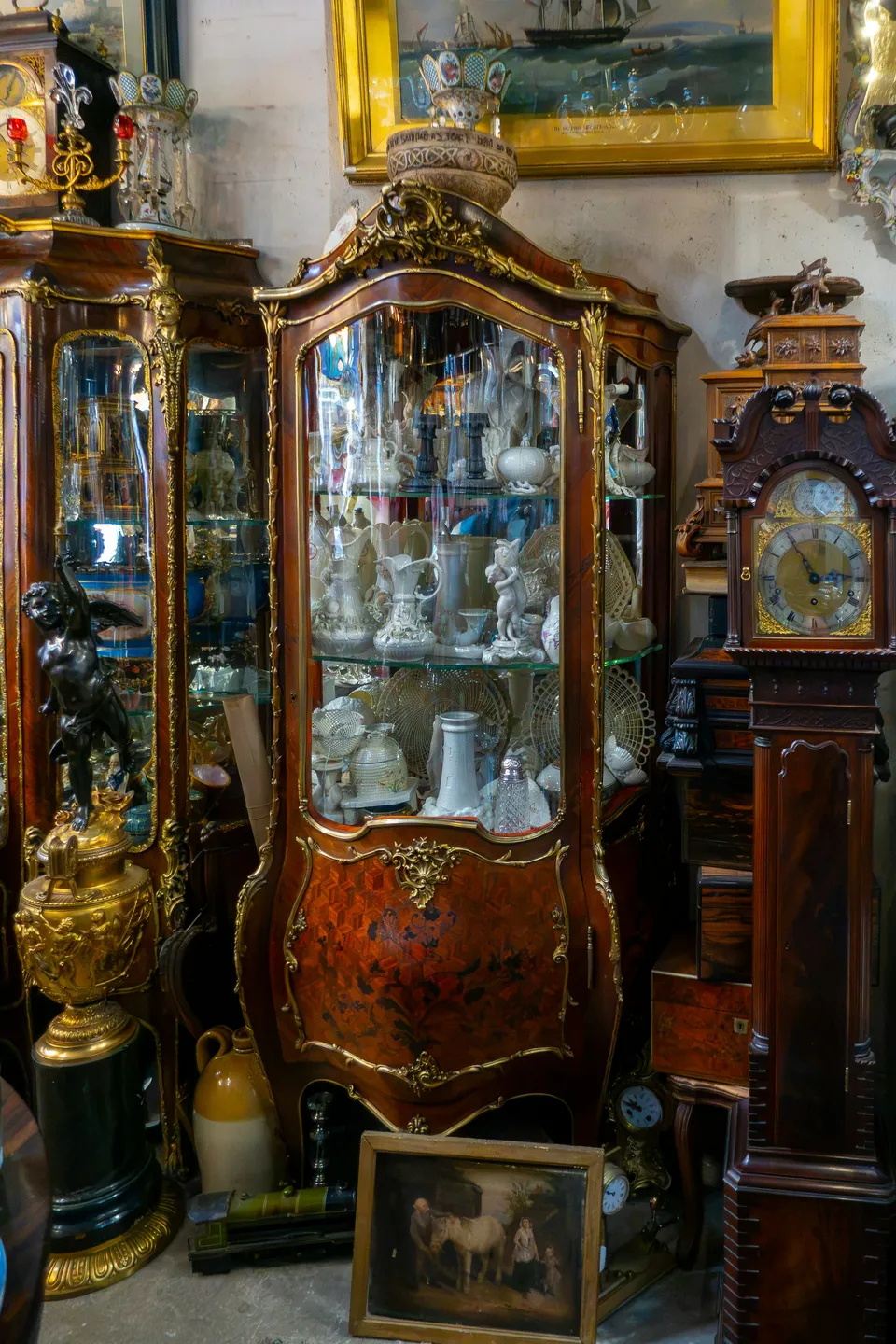 Antique glass-fronted cabinet holding porcelain, with a long-case clock beside it.
