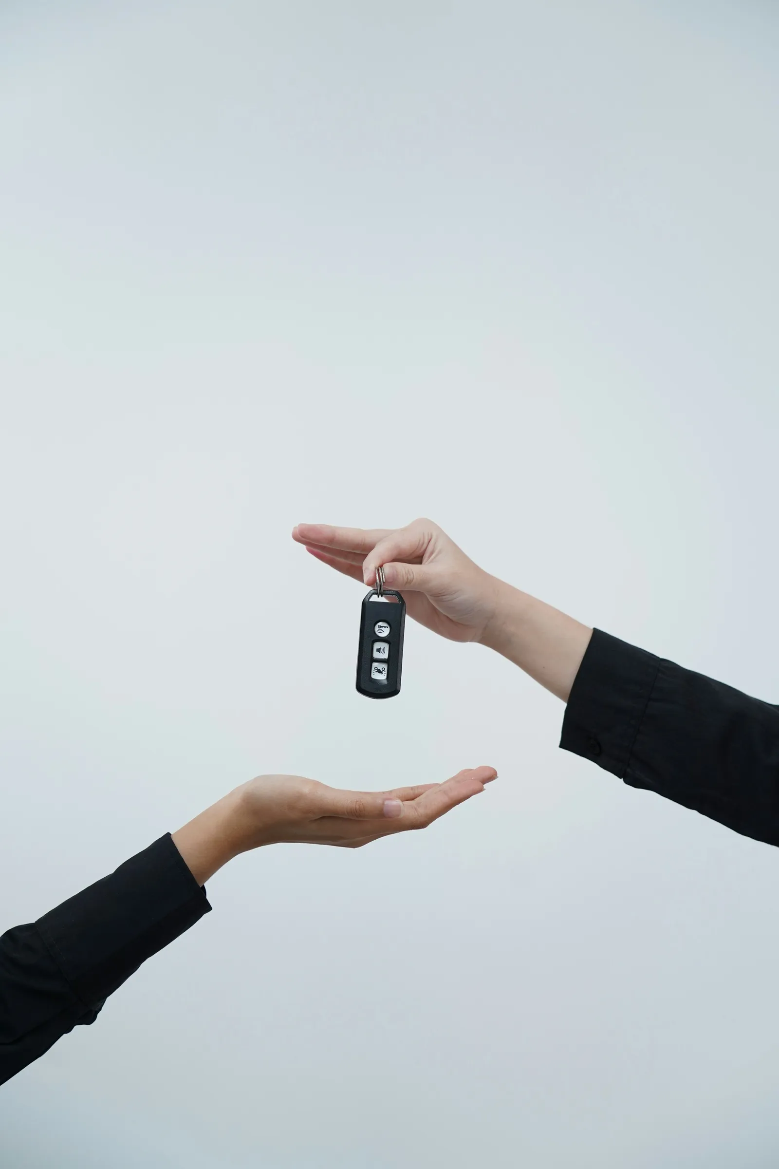 Two hands passing a car key to each other against a light background