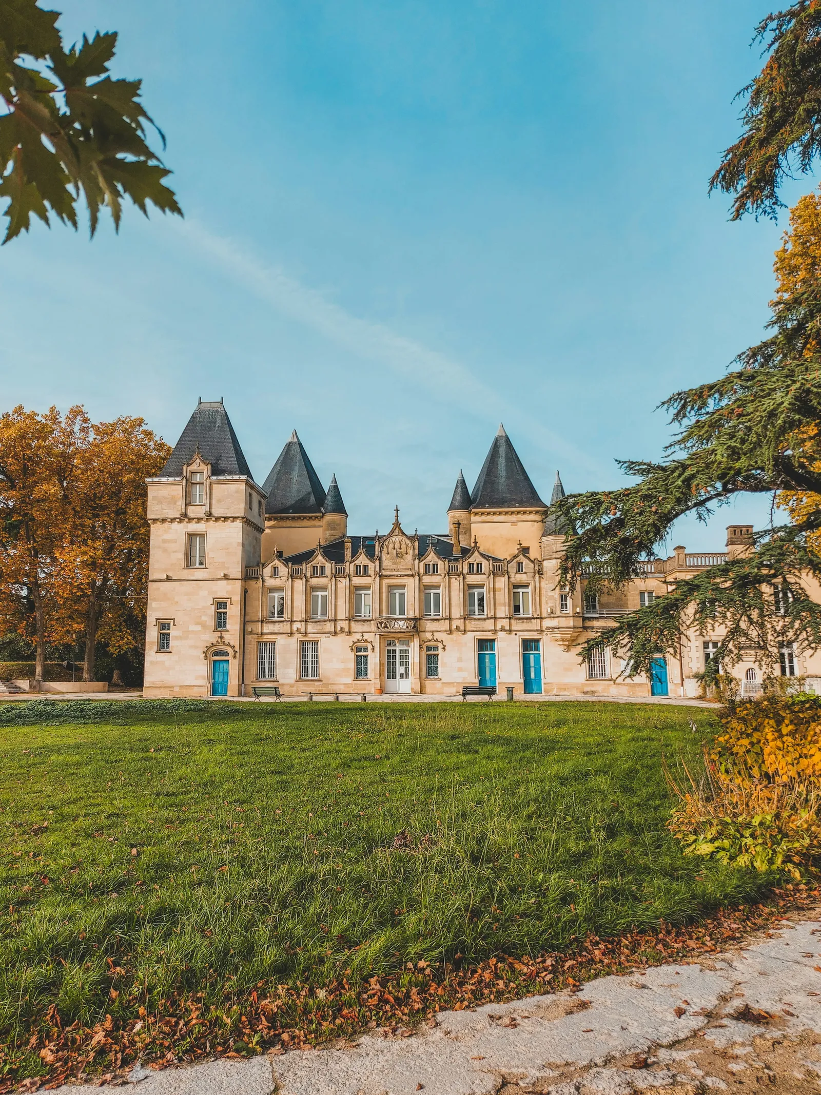 A stone château with slate-roofed corner towers and blue shutters, seen across a lawn in autumn light