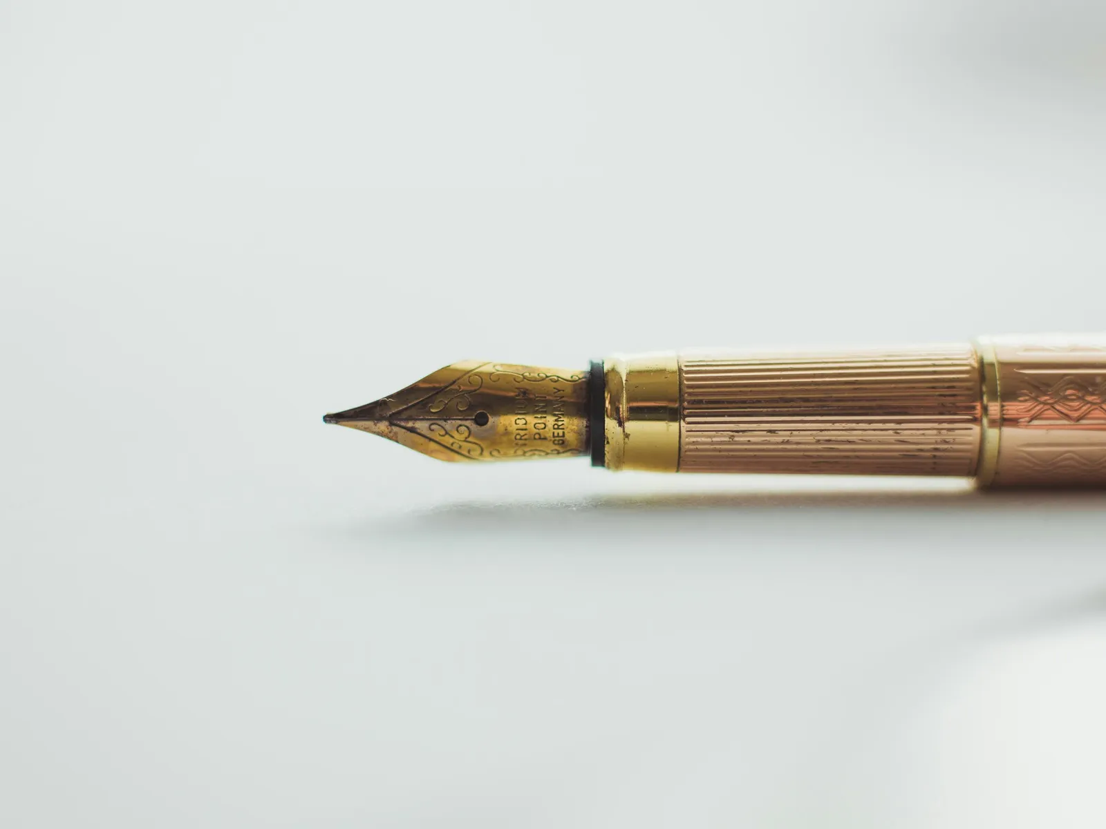 A gold fountain pen with an engraved nib lying on a white surface
