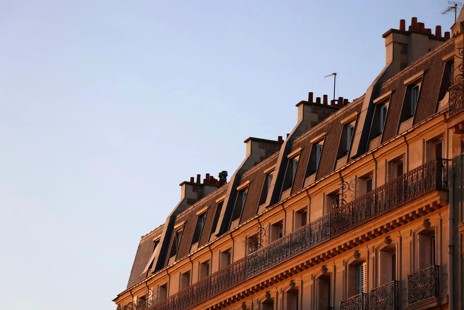 The upper floors of a Haussmann building in Paris with wrought-iron balconies and zinc roofs in warm evening light