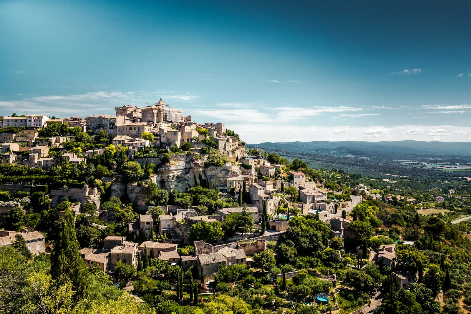 A hilltop village of stone houses above green hills in Provence