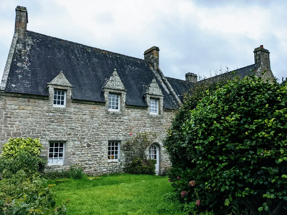 An old stone house with a slate roof, dormer windows and a lawn